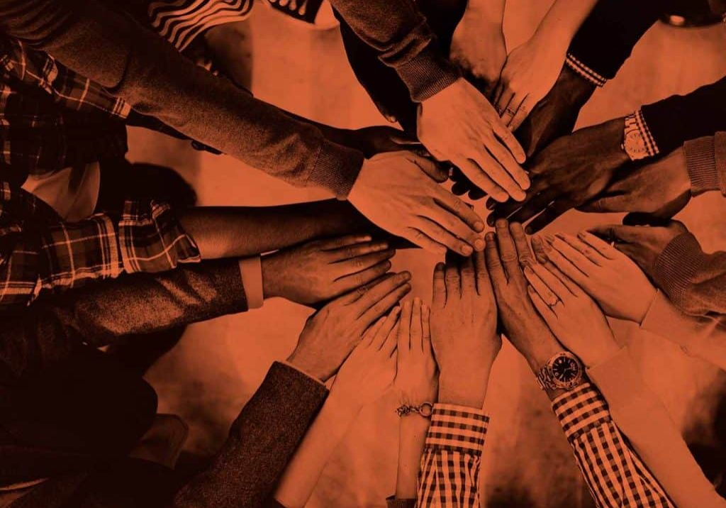 A group of people in a circle with their hands all together demonstrating team bonding